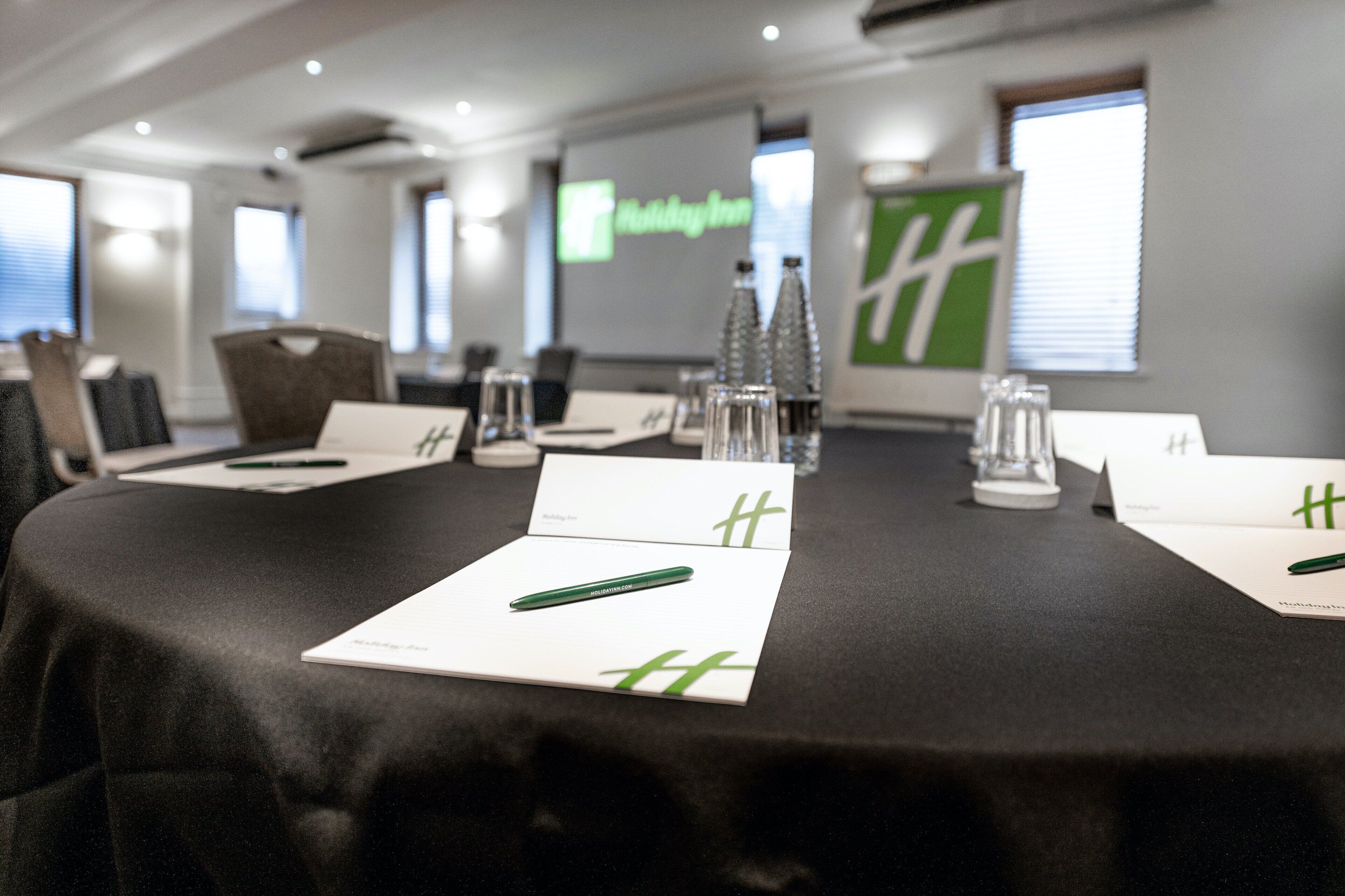 A conference room with a black table, white name cards, and a projector screen displaying "Holiday Inn".