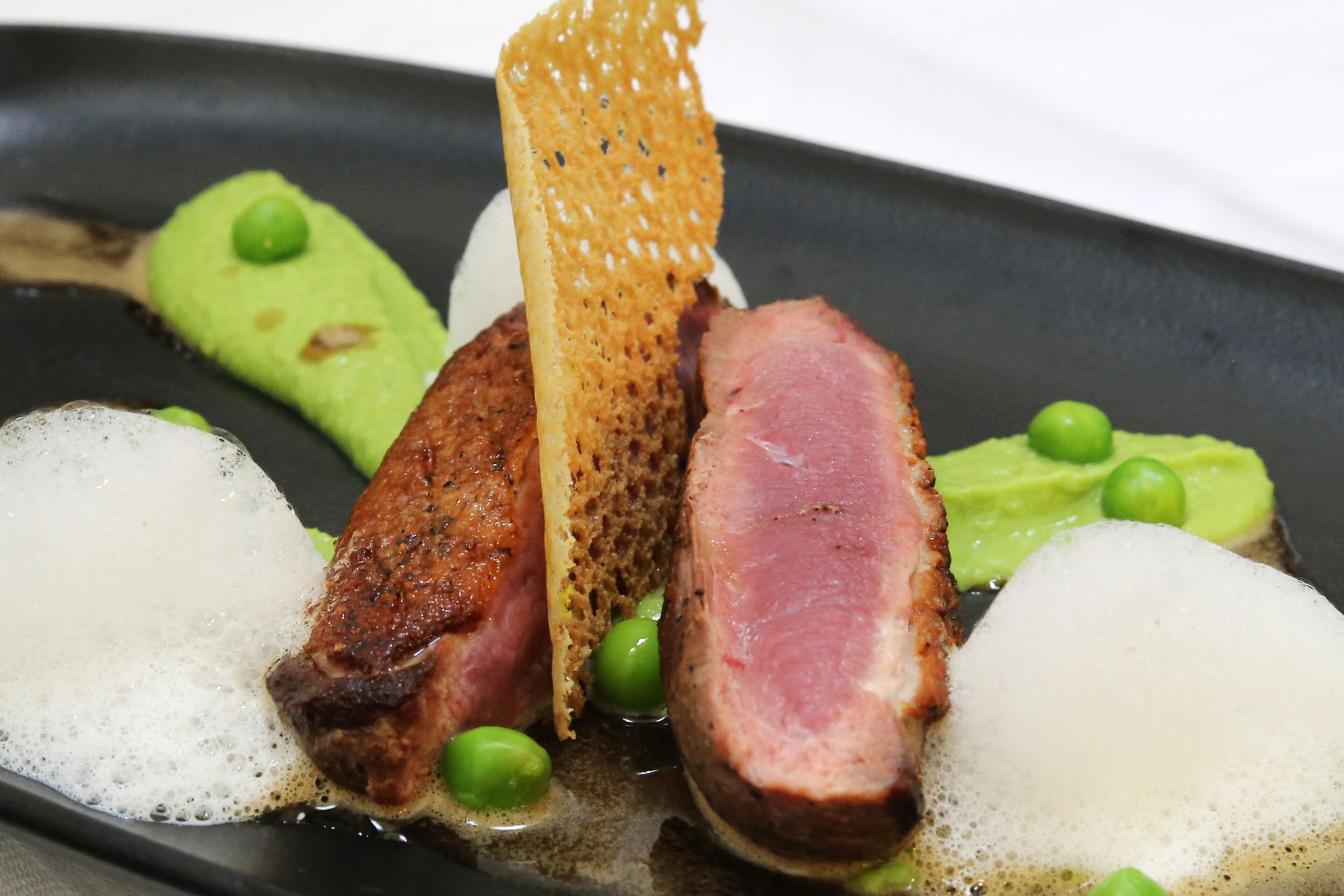 A dish with various food items including meat, peas, and a piece of bread.