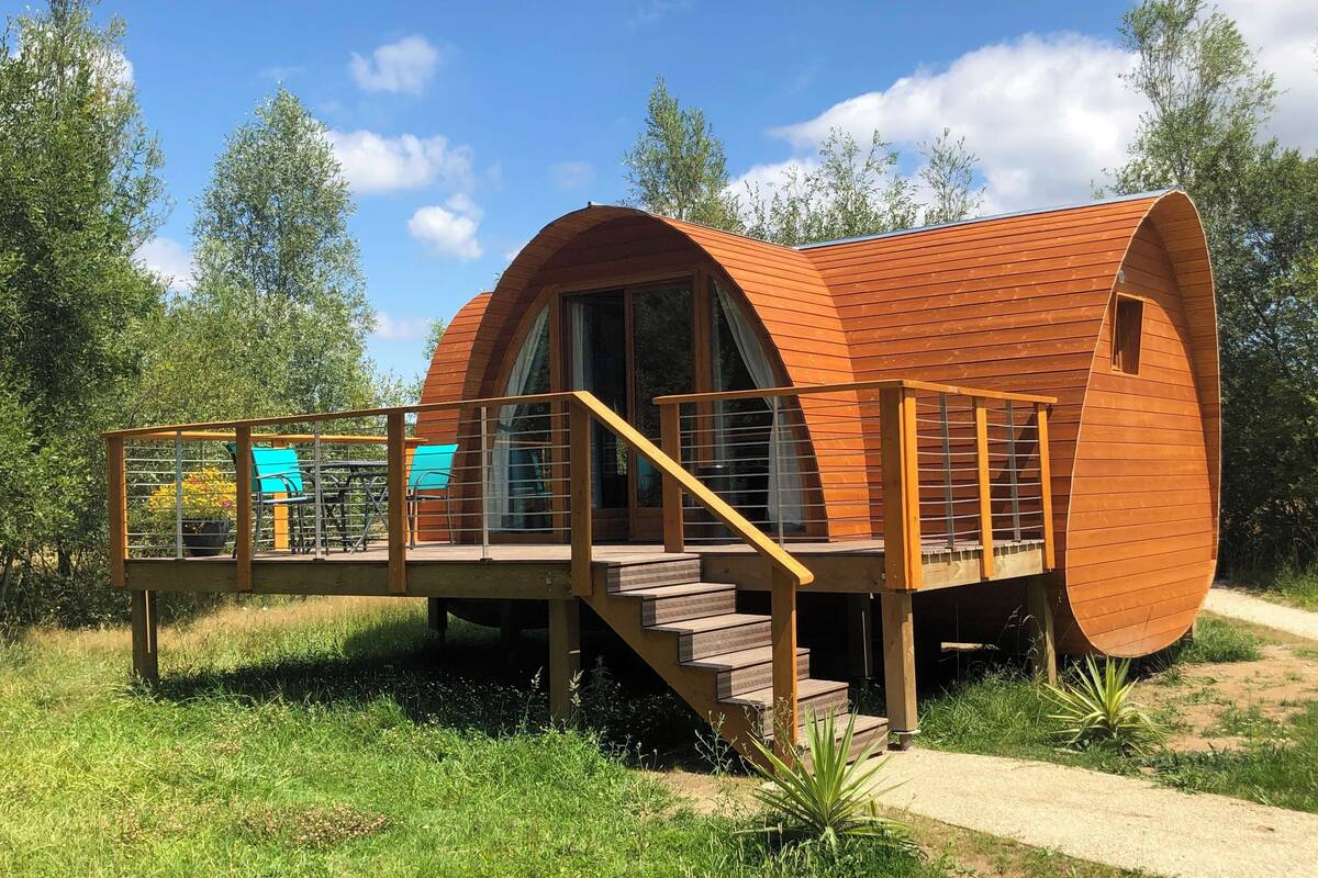 A wooden pod-style cabin with a deck and stairs, surrounded by greenery.