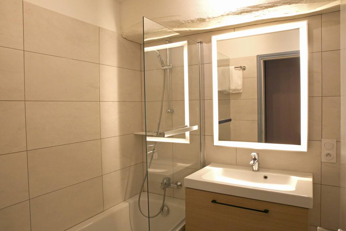 A modern bathroom with a glass-enclosed shower, a white sink, and a mirror with integrated lighting.