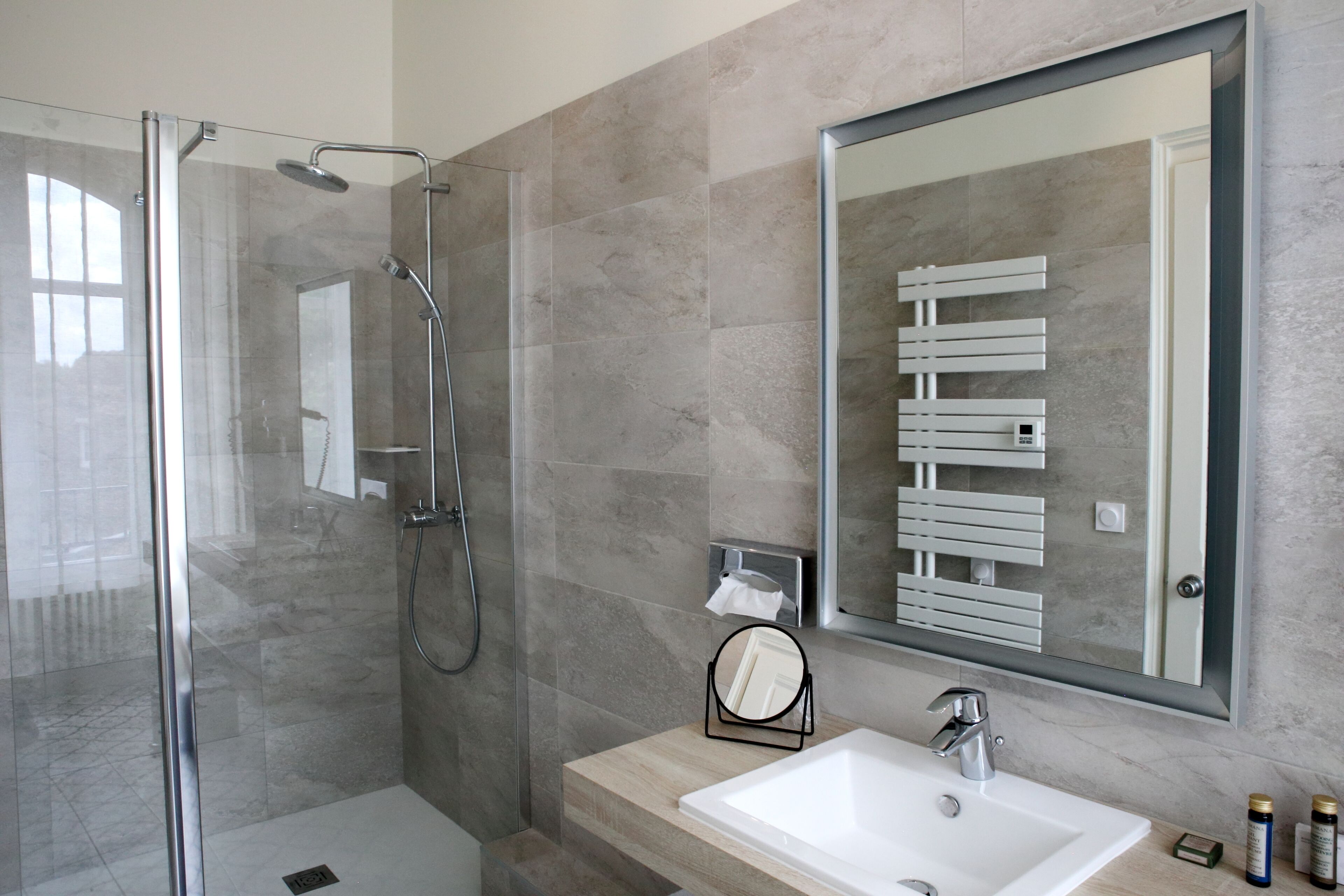A modern bathroom with a glass-enclosed shower, a white sink, and a large mirror.