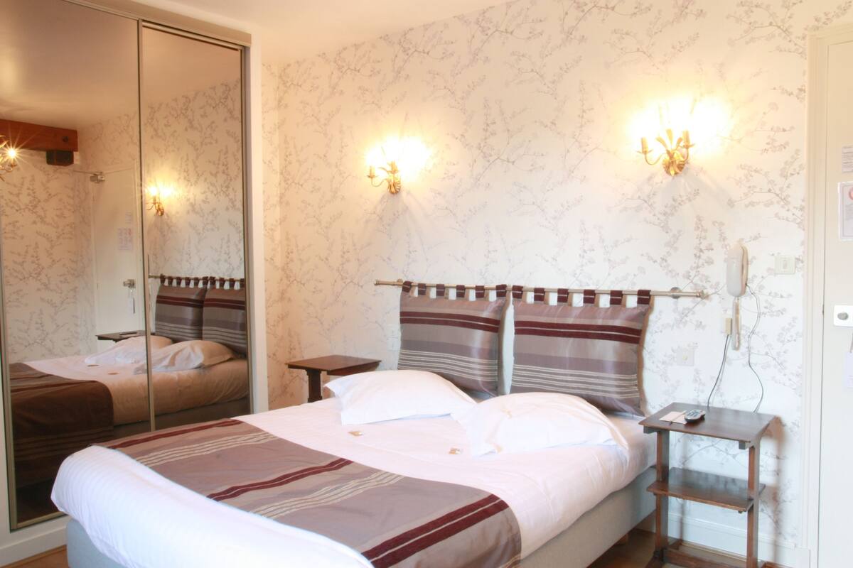 A hotel room with a bed, bedside tables, a mirror, and wall-mounted lights.