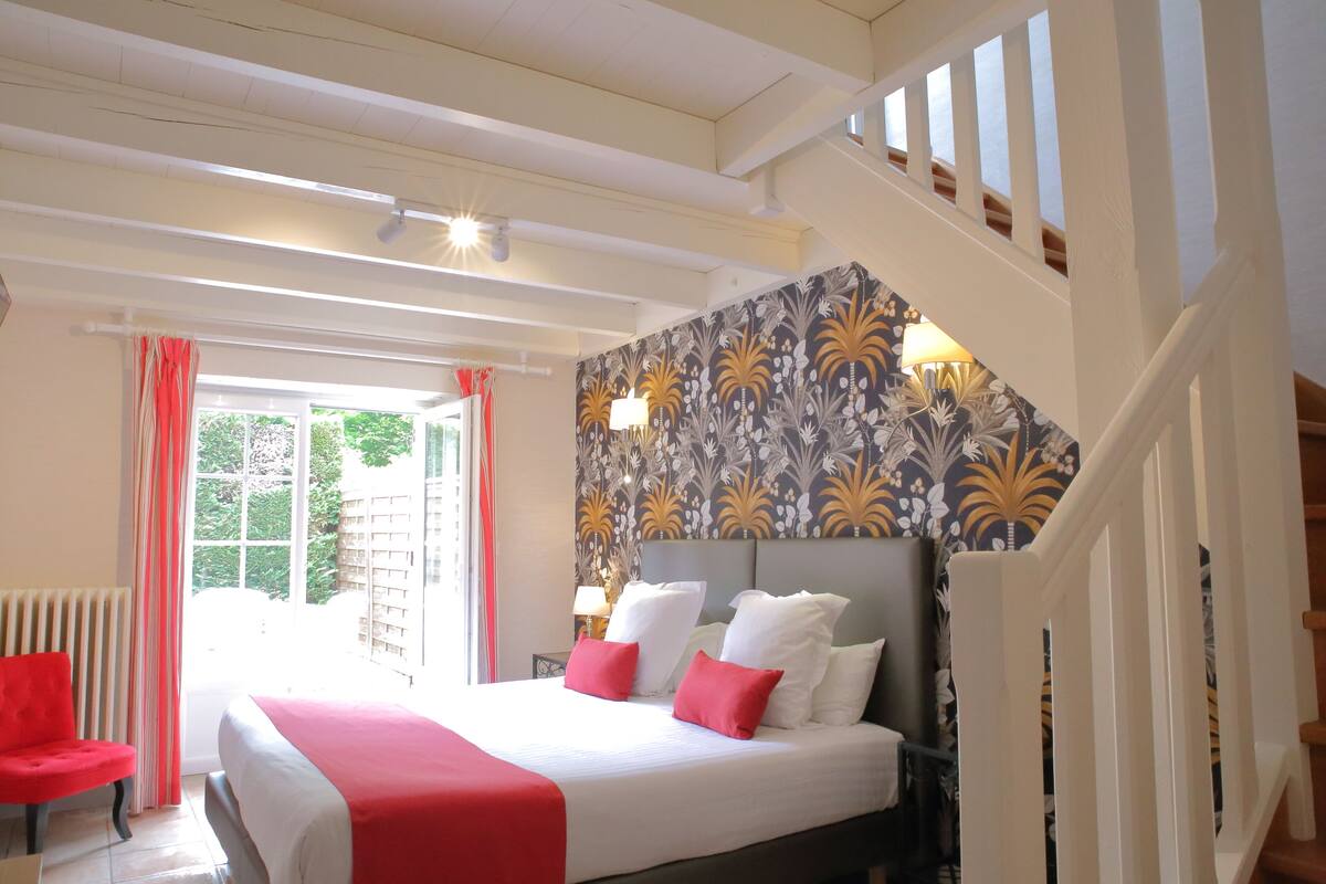 A hotel room with a large bed, red chair, and a staircase.