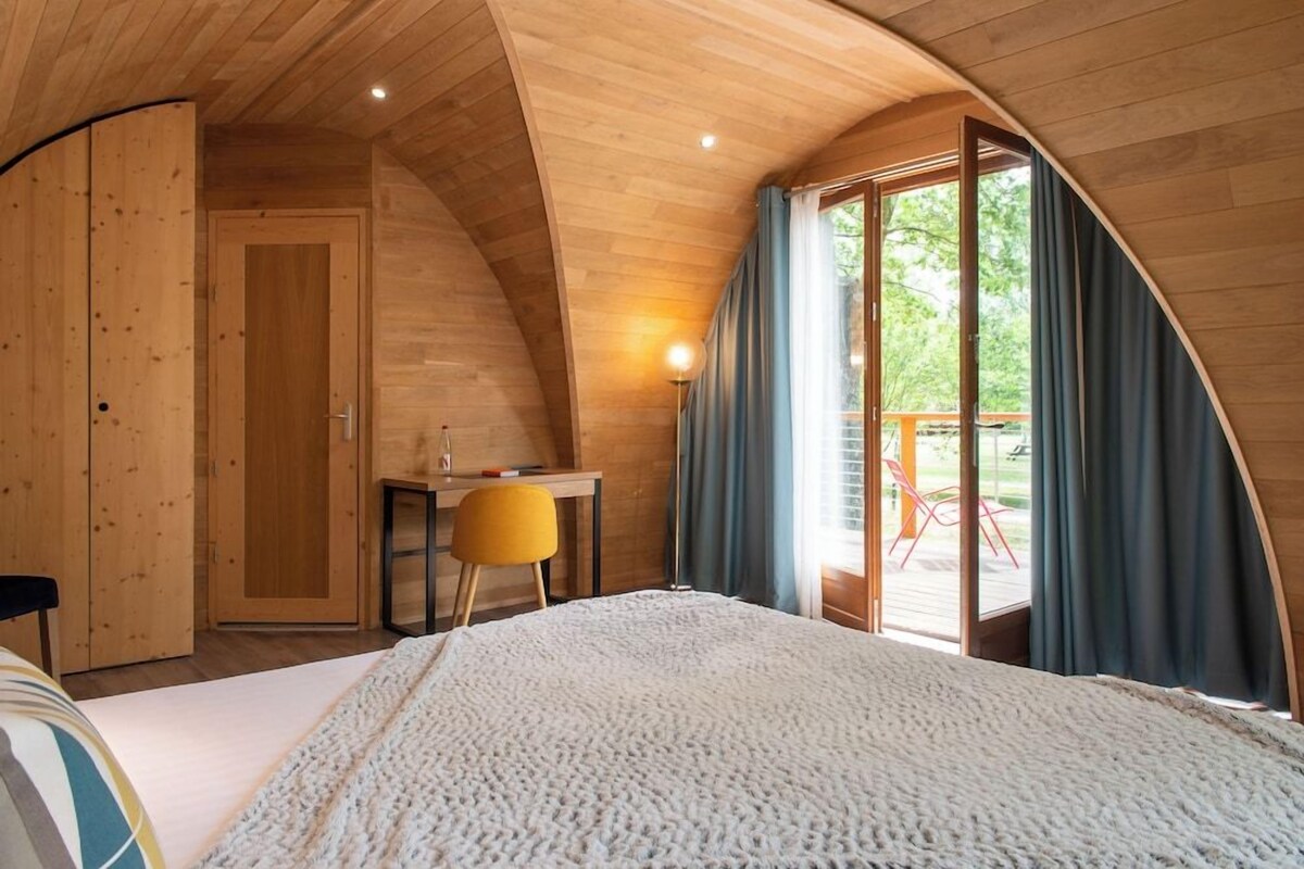 A cozy bedroom with a large bed, wooden walls, a desk, and a view of the outdoors.