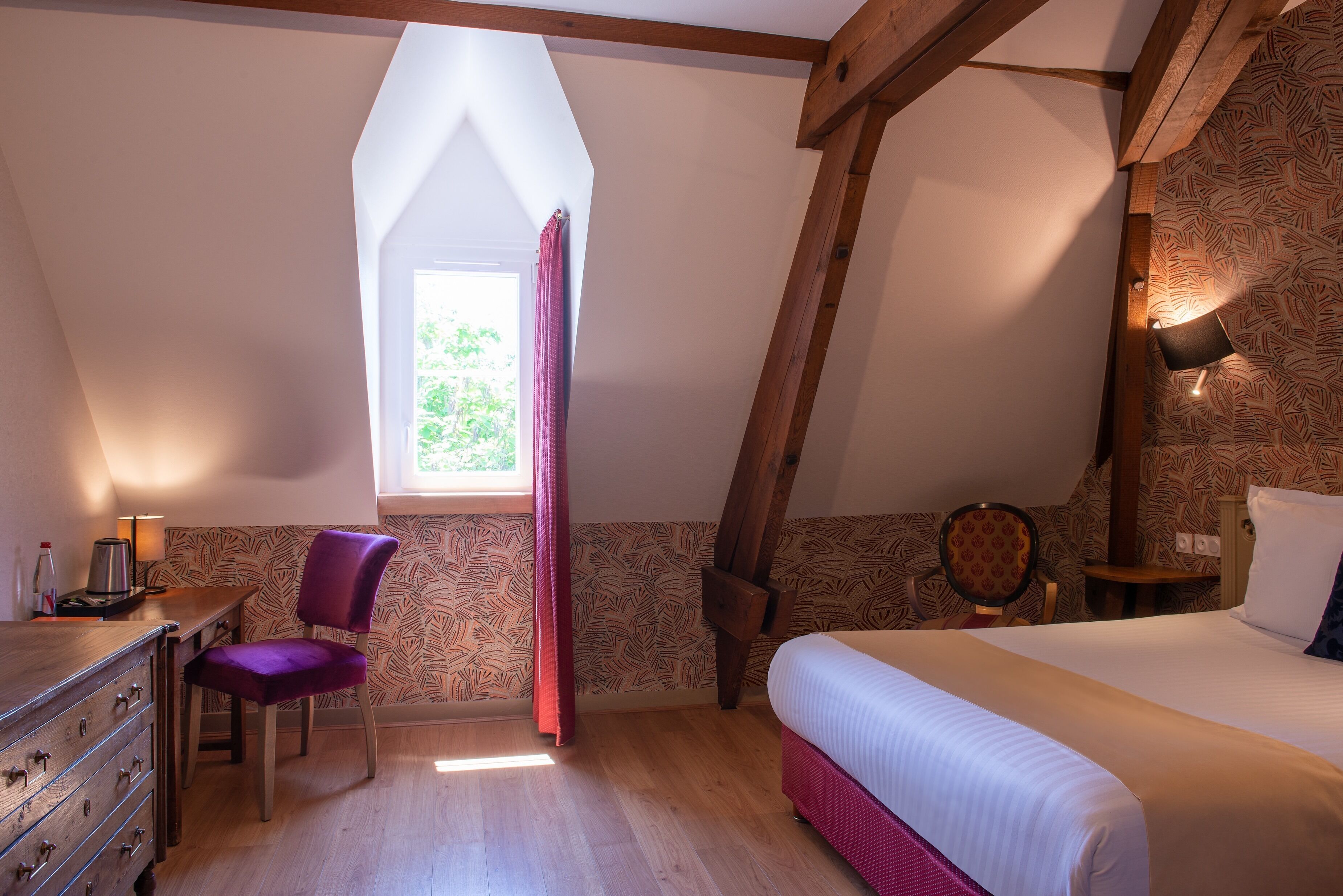 A bedroom with a wooden ceiling, a bed, a chair, a desk, and a window with a curtain.