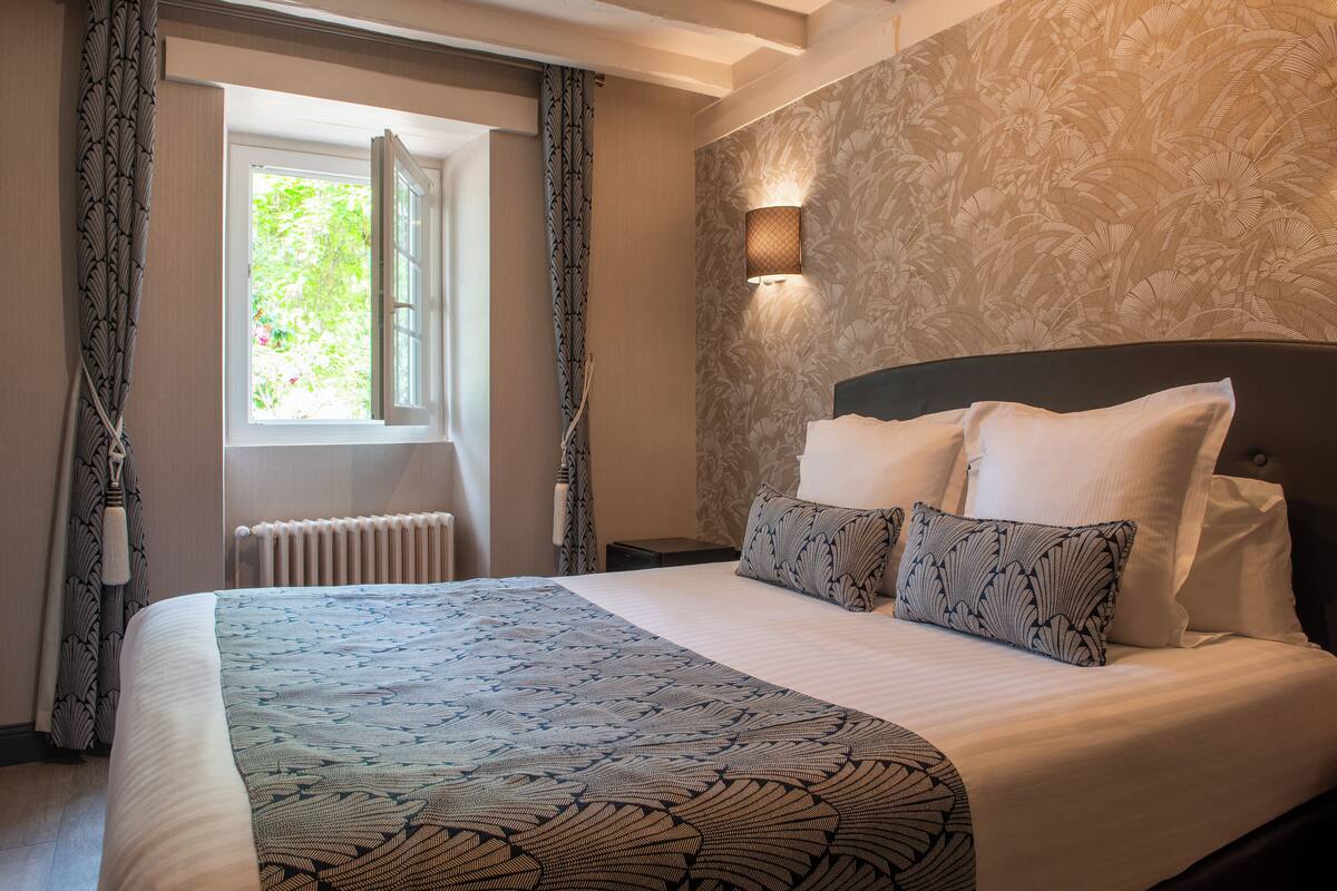 A hotel room with a large bed, a window with curtains, a wall-mounted light, and a radiator.