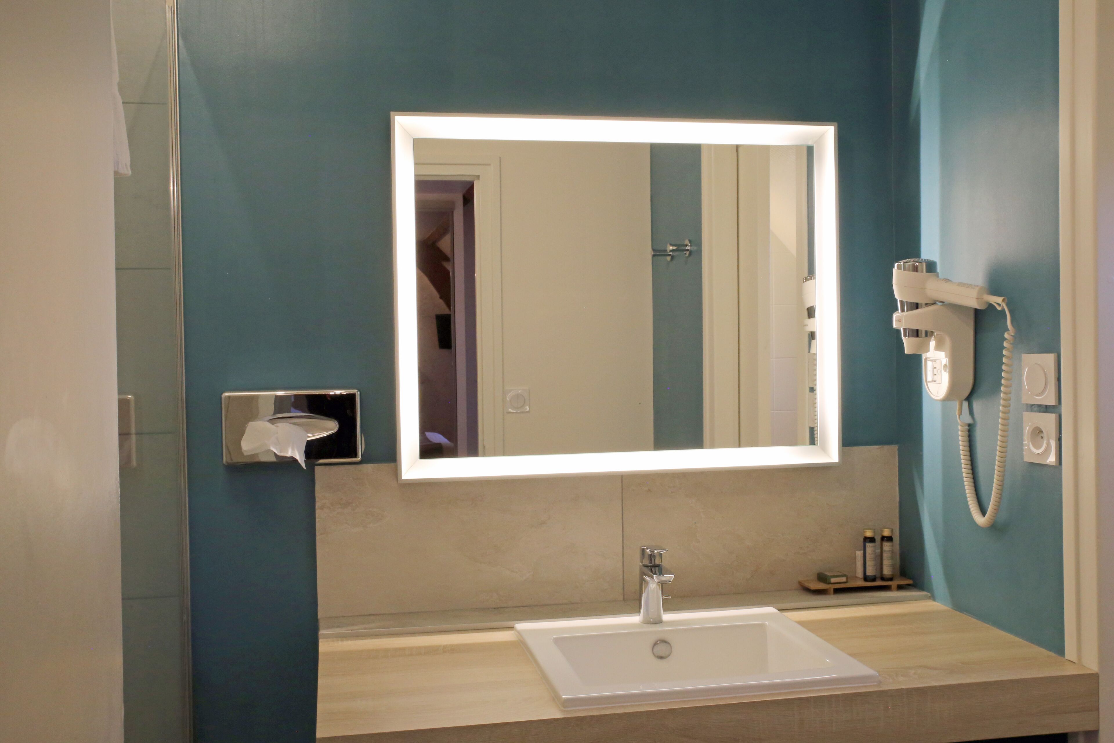 A bathroom with a large mirror, a sink, and a hairdryer on the wall.