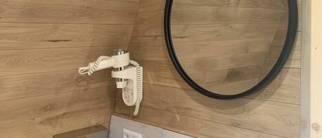 Ein Badezimmer mit Holzwandverkleidung, einem runden Spiegel, einem weißen Waschbecken und einem Handtuchhalter.