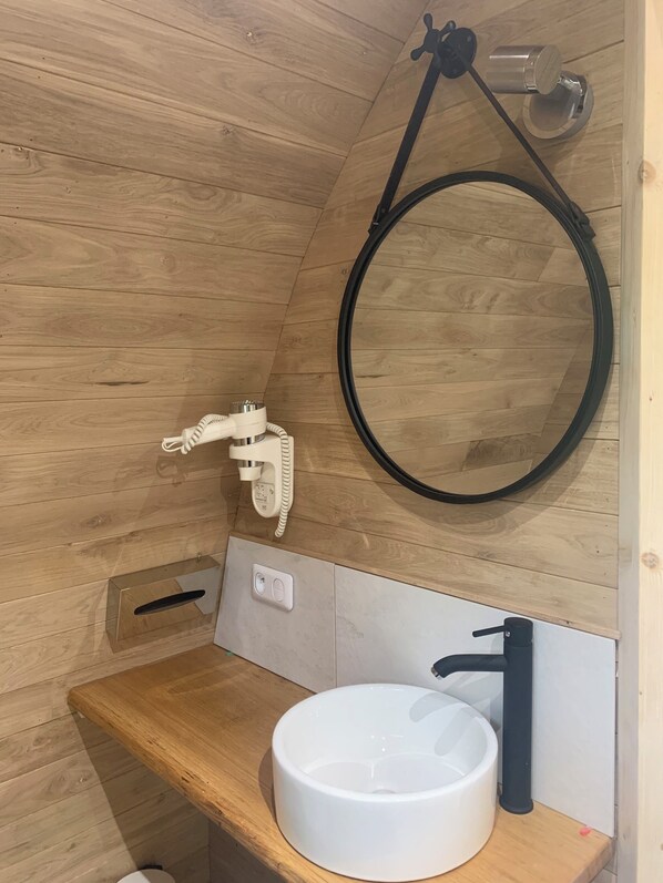 A wooden-paneled bathroom with a round mirror, a white sink, and a towel rack. - Hôtel Relais des Landes - Demeures et Châteaux (Le Controis en Sologne)