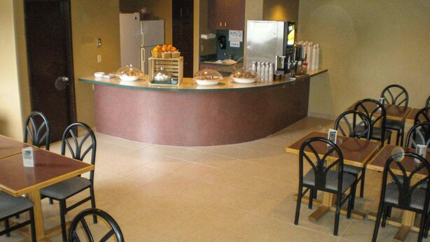 Een ontbijtbuffet met afgedekte schalen, een koelkast en een koffieapparaat in een hotelrestaurant.