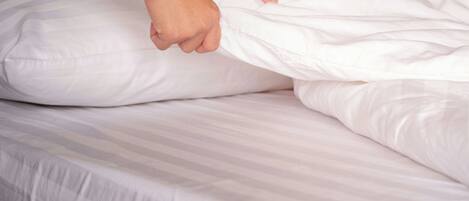 A bed with white bedding and a striped sheet.