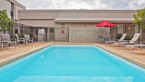 A rectangular swimming pool with a tiled deck surrounding it. There are lounge chairs and a red umbrella on the deck. - Holiday Inn Bloomington-University Area by IHG (Bloomington)