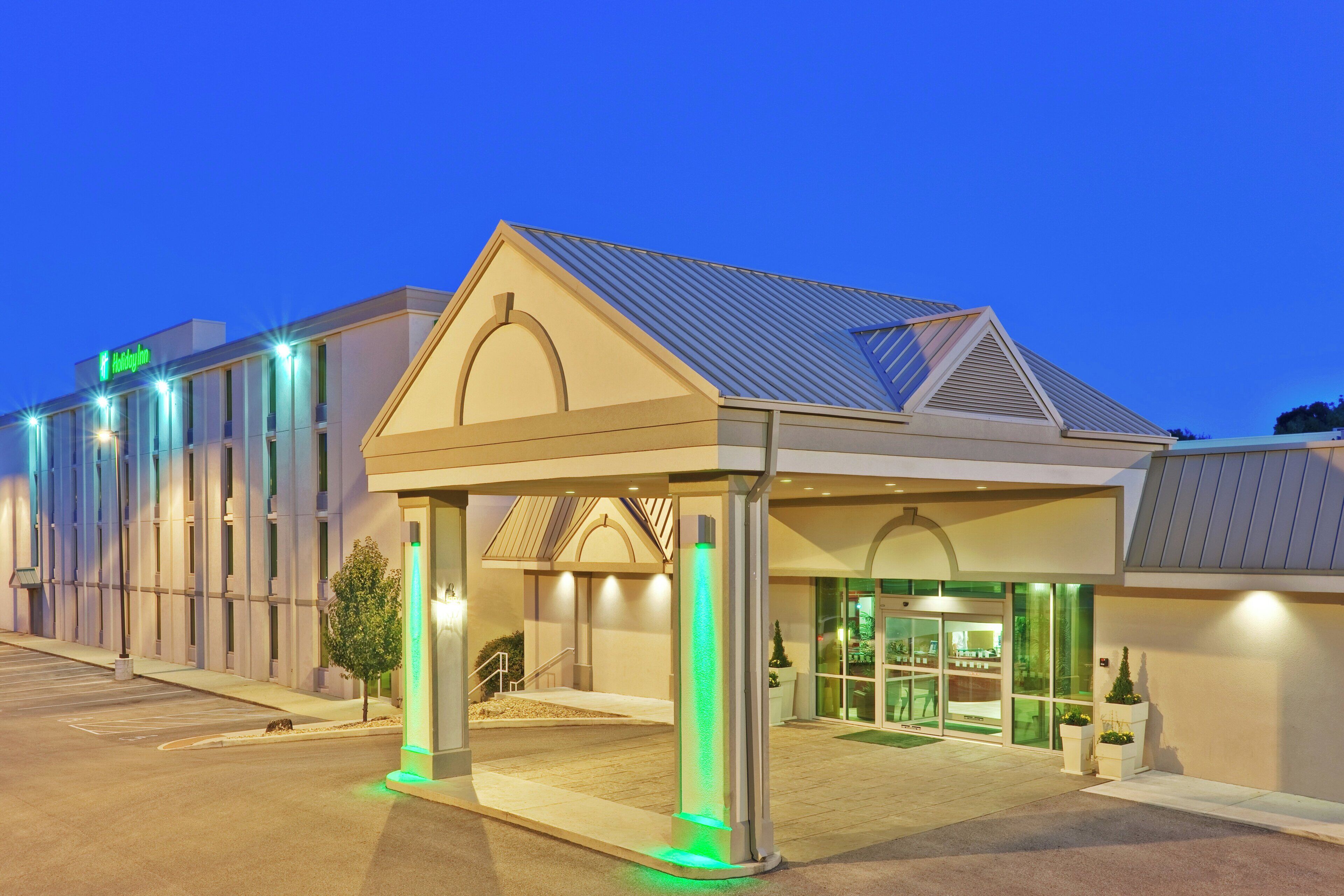 A Holiday Inn hotel with a covered entrance, a parking lot, and a building with a metal roof.