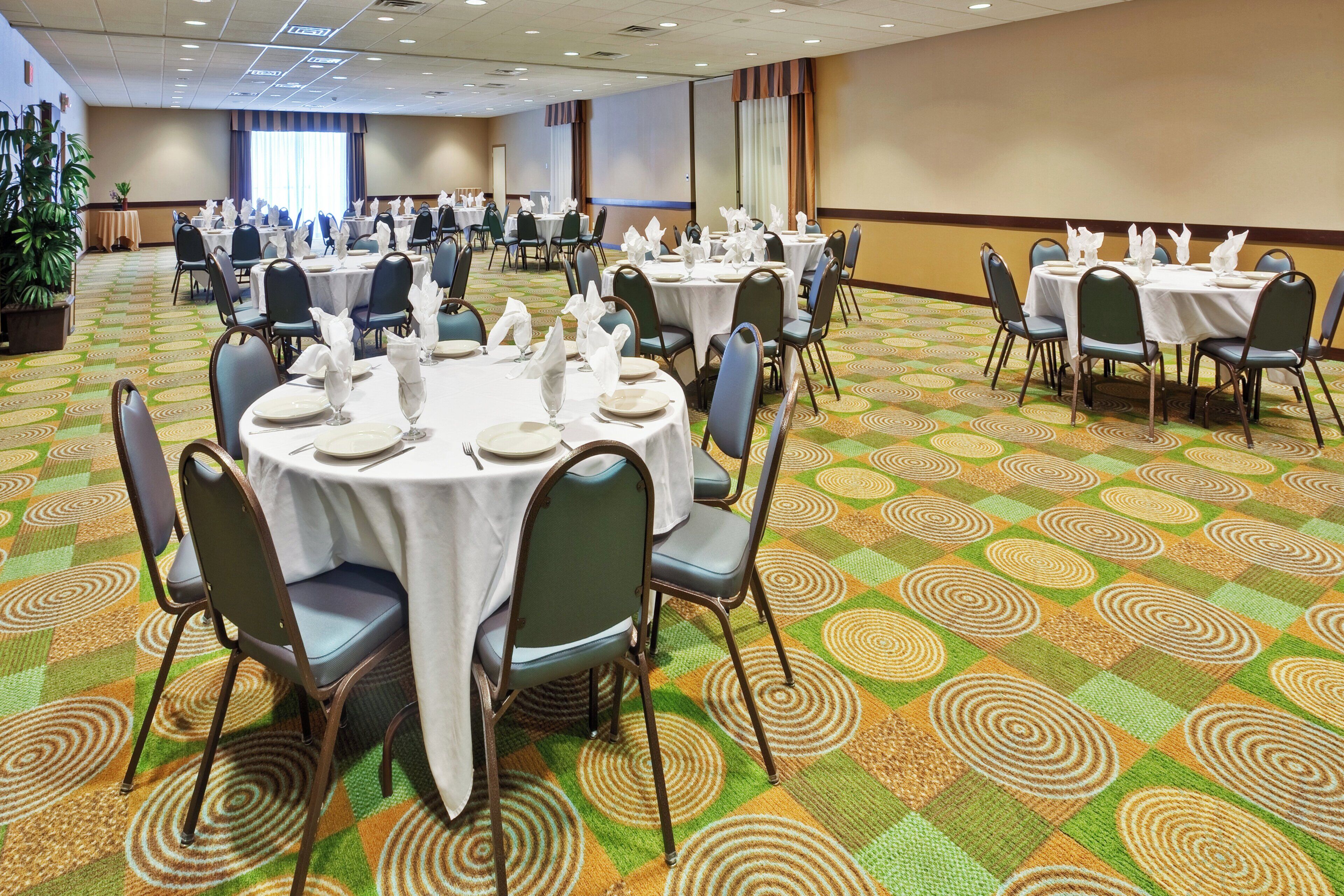 A hotel conference room with round tables, chairs, and a patterned carpet.