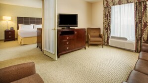 Une chambre d’hôtel avec un lit, un téléviseur posé sur une commode en bois, une chaise et une grande fenêtre avec des rideaux.