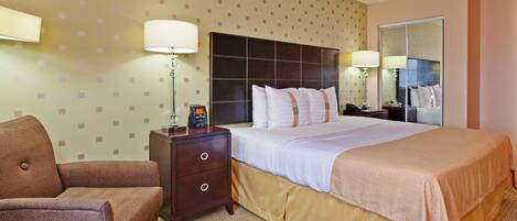 Une chambre d’hôtel avec un lit, une table de chevet, une lampe, une chaise et un miroir.