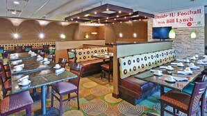A restaurant with booths and tables, a banner, and a television. - Holiday Inn Bloomington-University Area by IHG (Bloomington)