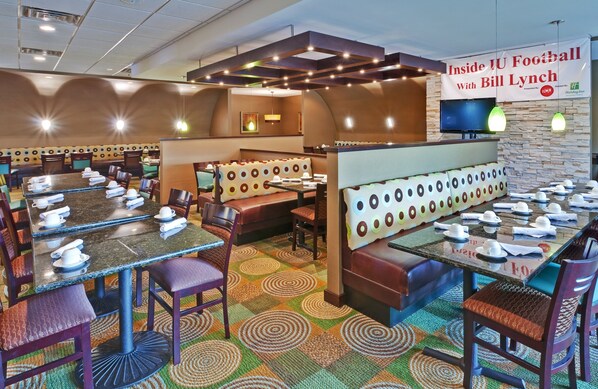 Un restaurant avec des banquettes et des tables, une enseigne et un téléviseur.