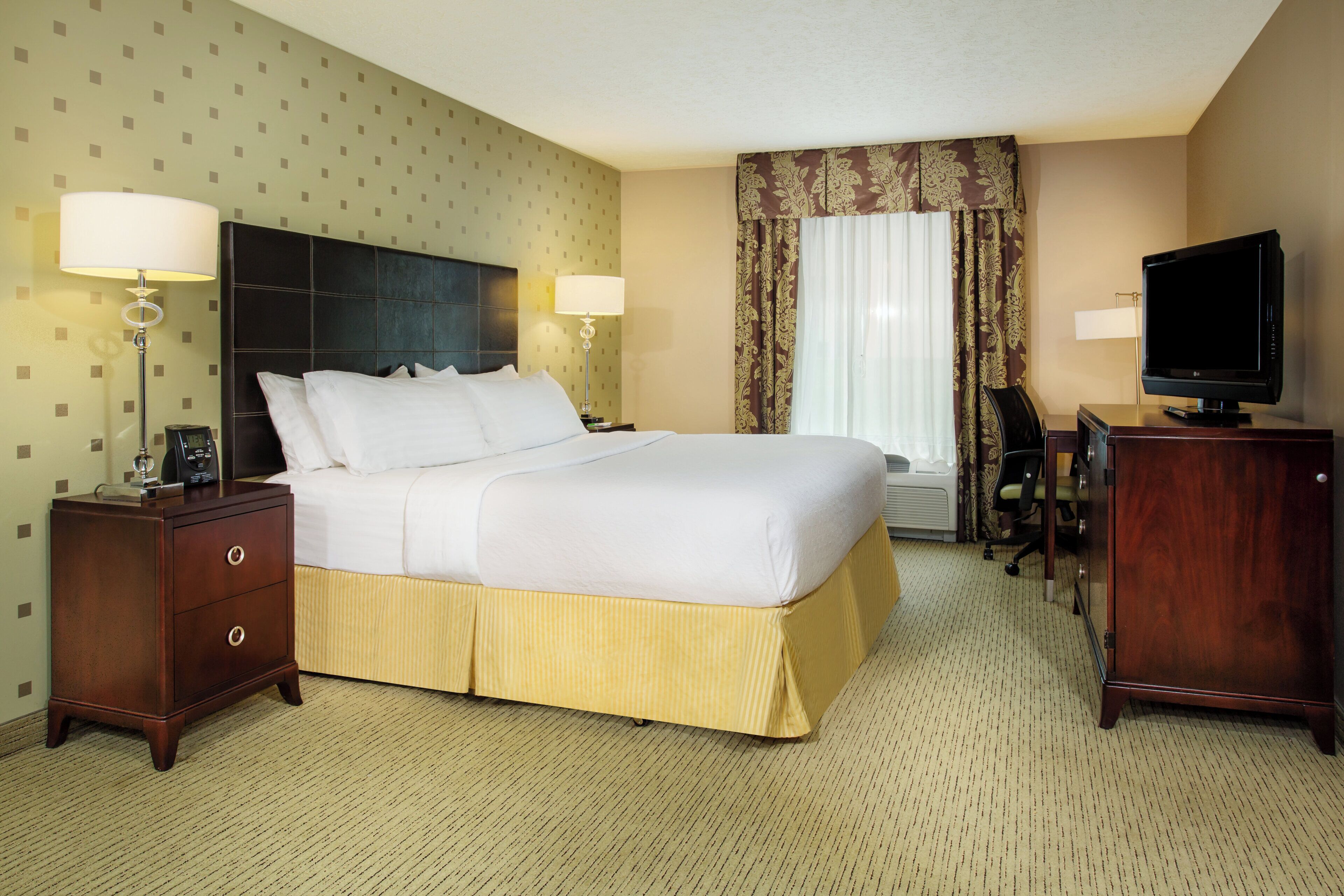 A hotel room with a bed, two bedside tables, a desk with a chair, a television, and a window with curtains.
