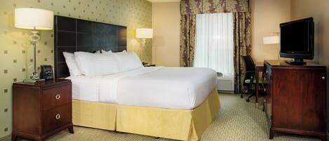 A hotel room with a bed, two bedside tables, a desk with a chair, a television, and a window with curtains.