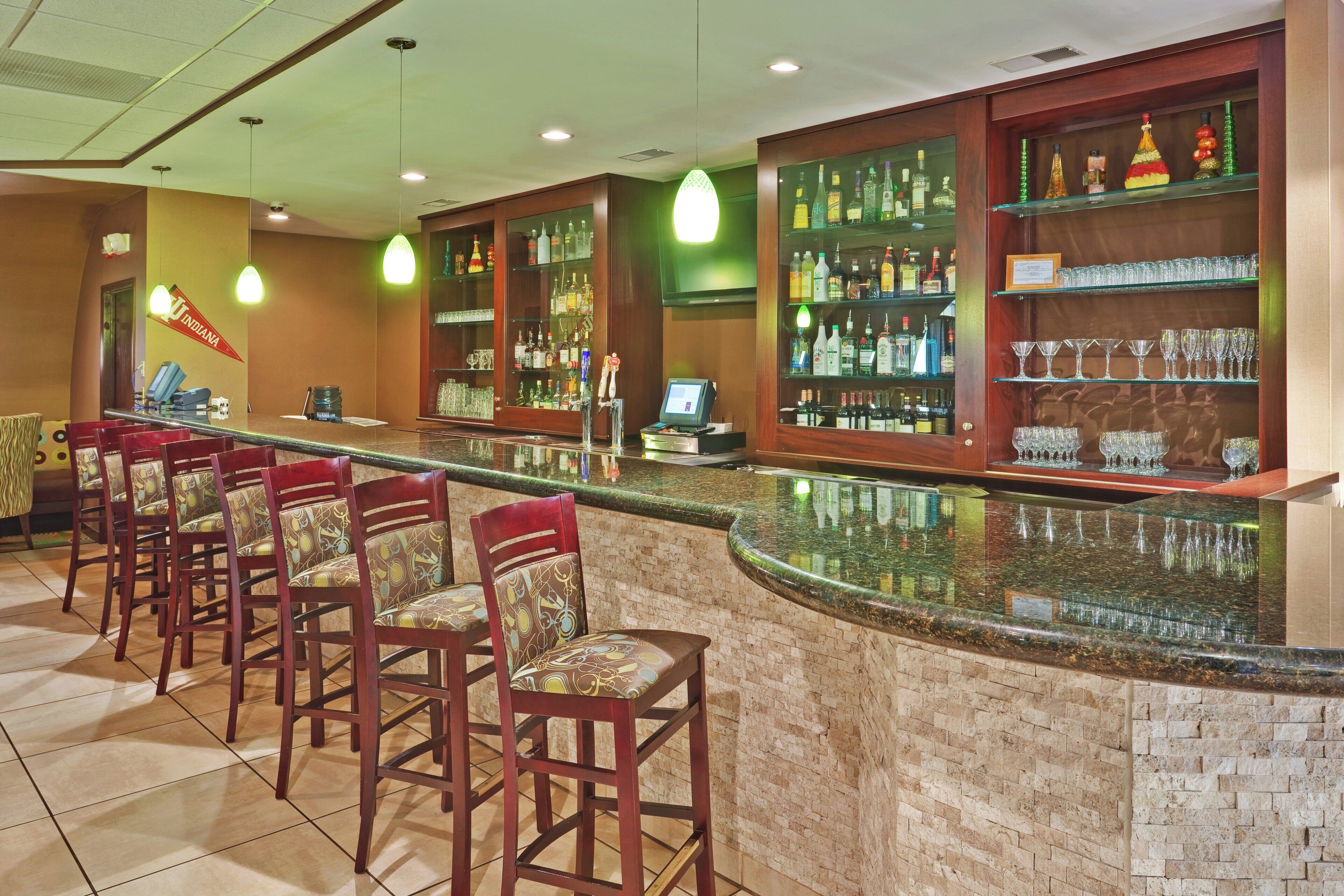 A bar area with a counter, multiple stools, and shelves stocked with bottles and glasses.