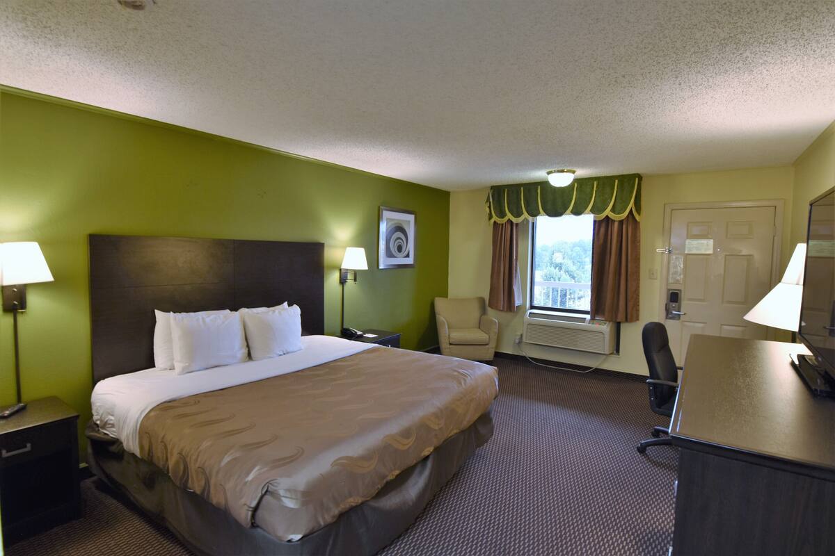 Une chambre d’hôtel avec un grand lit, un bureau, une chaise et une fenêtre avec des rideaux.