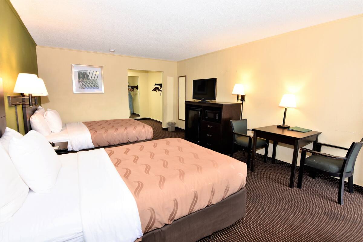 Une chambre d’hôtel avec deux lits, un bureau, une chaise, une télévision et un miroir.