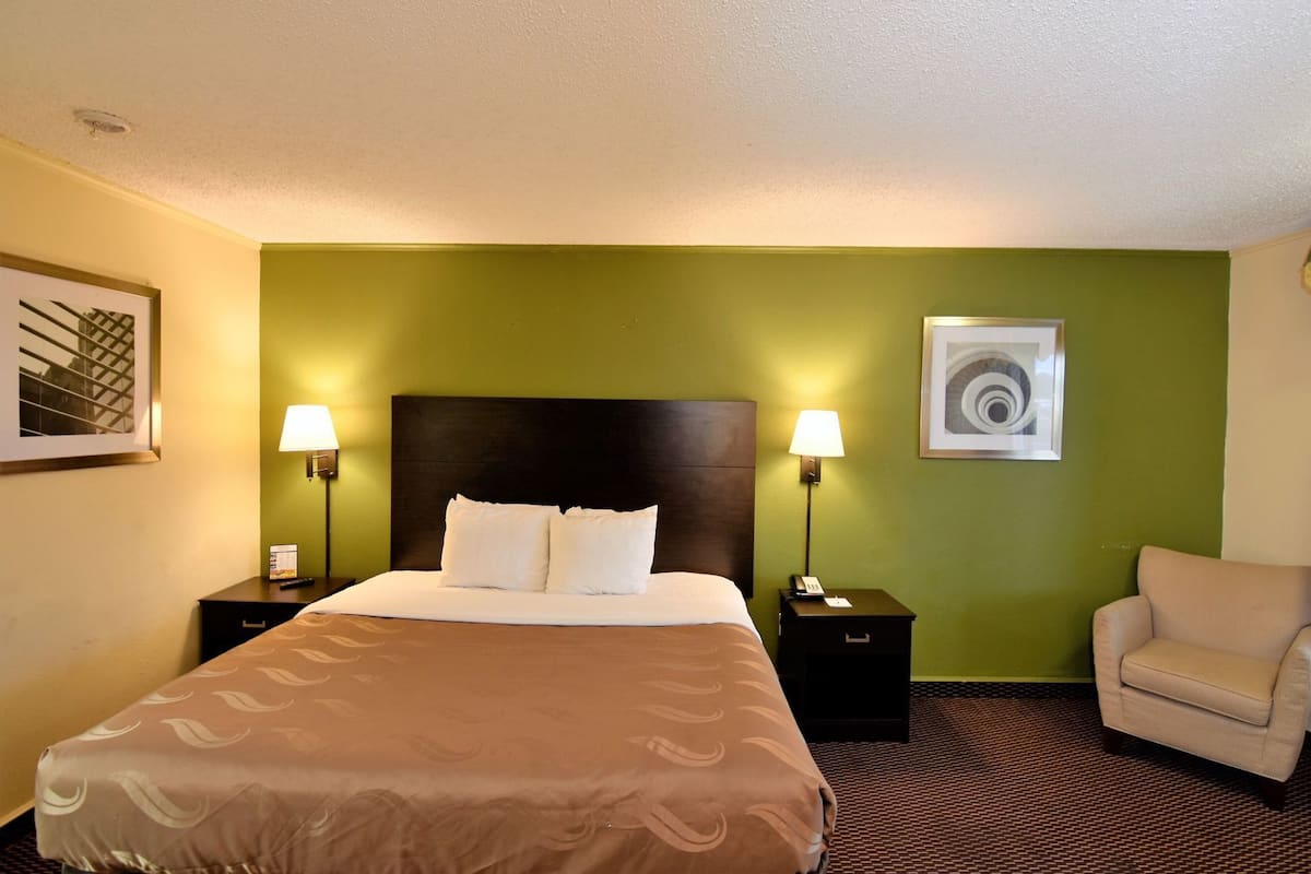 A hotel room with a bed, two bedside tables, a chair, and a wall with a framed picture.