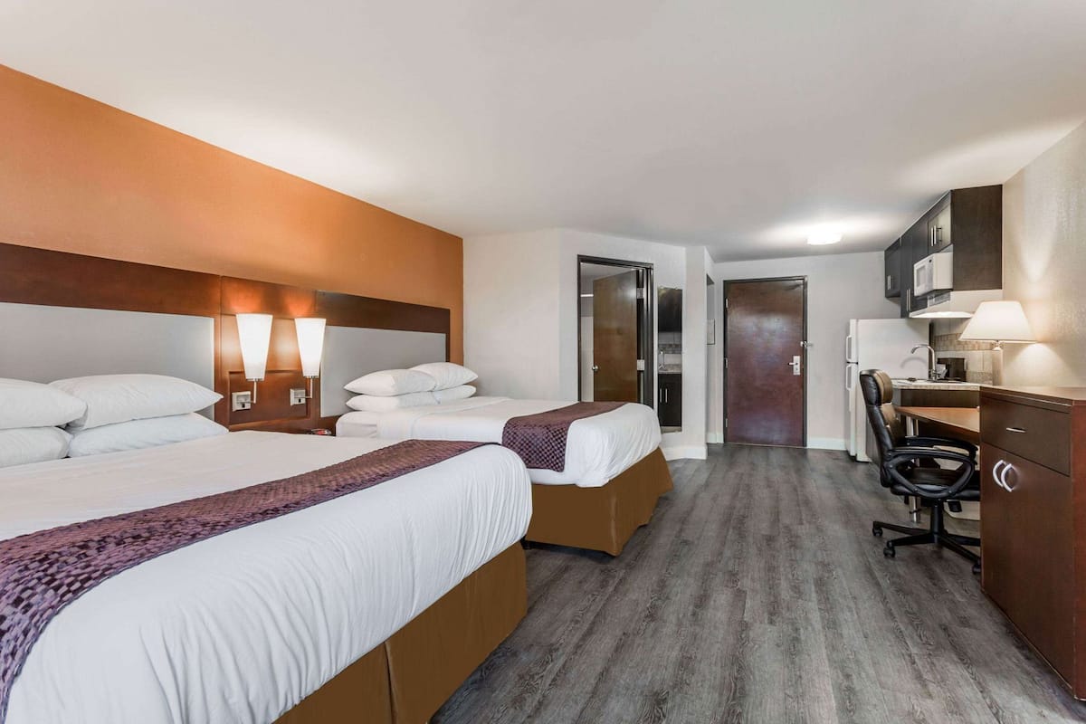 Ein Hotelzimmer mit zwei Betten, einem Schreibtisch, einem Stuhl, einem Kleiderschrank und einem Badezimmer.