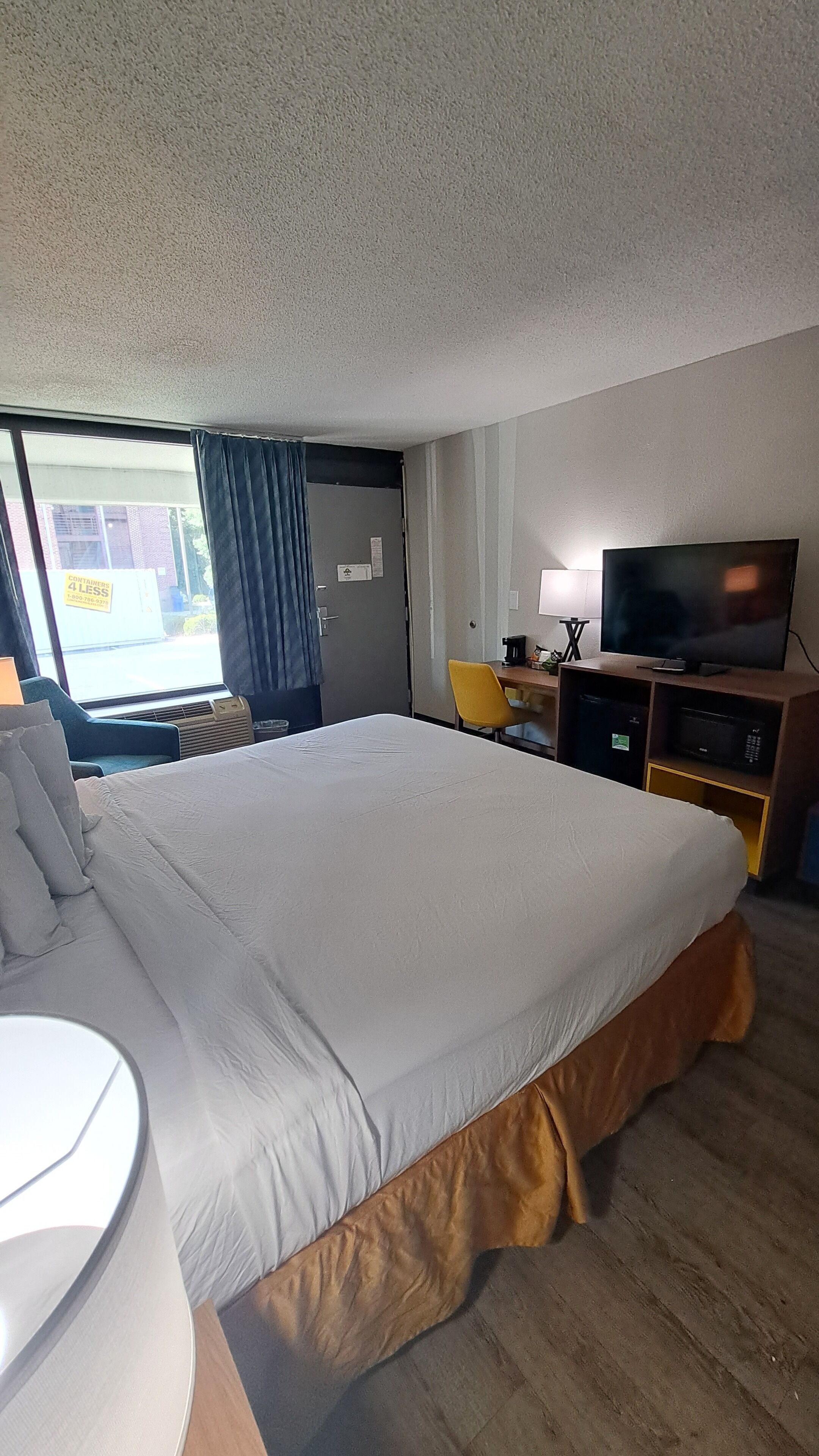 Habitación de hotel con una cama grande, un escritorio con silla, televisor y ventana con cortinas.
