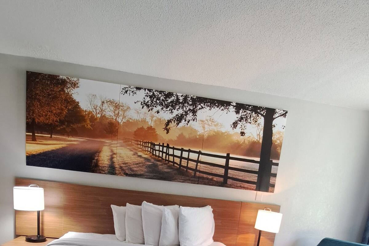 Ein Hotelzimmer mit einem großen Bett, einem Kopfteil mit einem Gemälde, zwei Nachttischen mit Lampen und einem blauen Sessel.