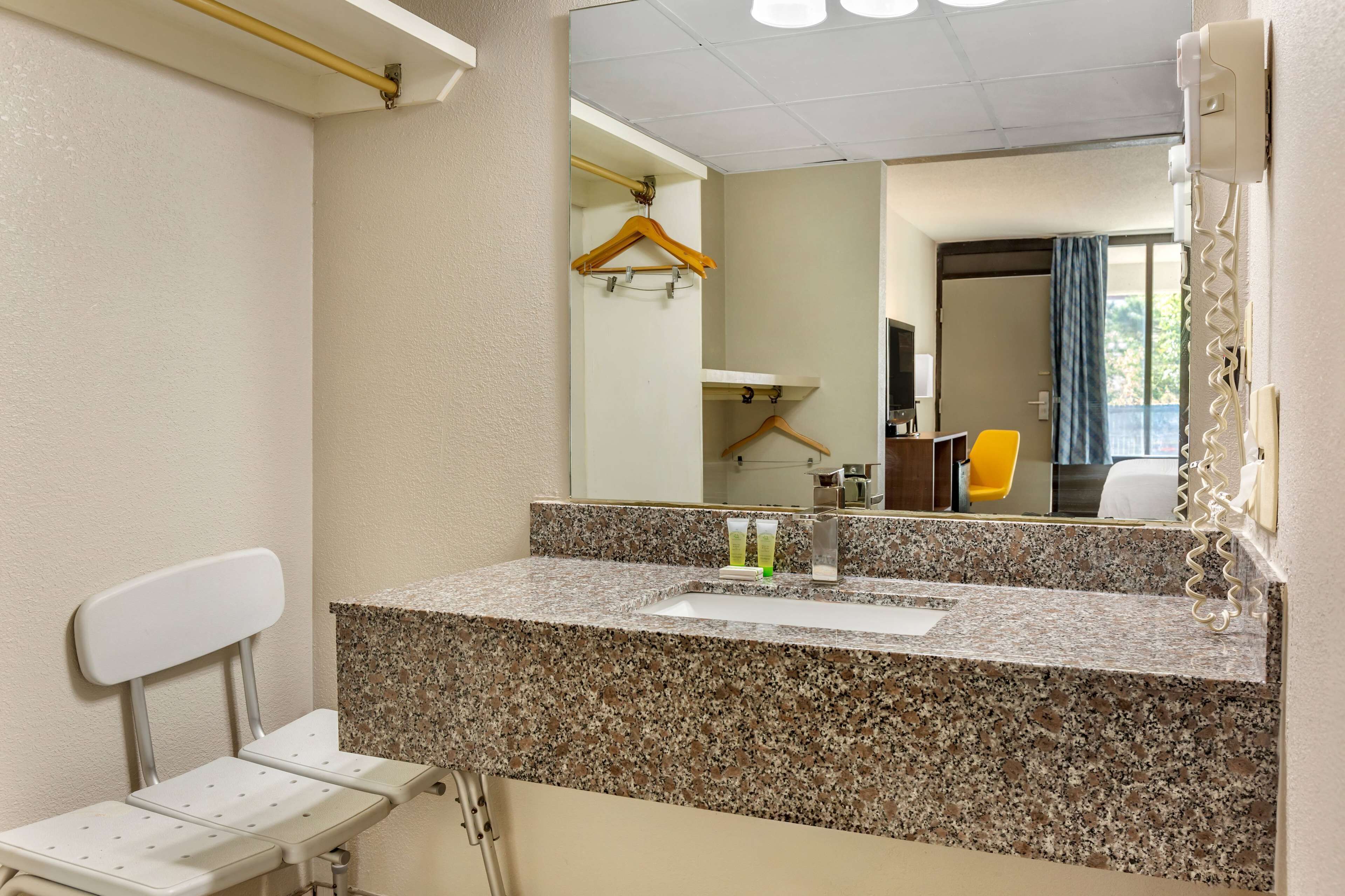 A bathroom with a granite countertop, a white chair, a mirror, and a yellow chair visible in the reflection.