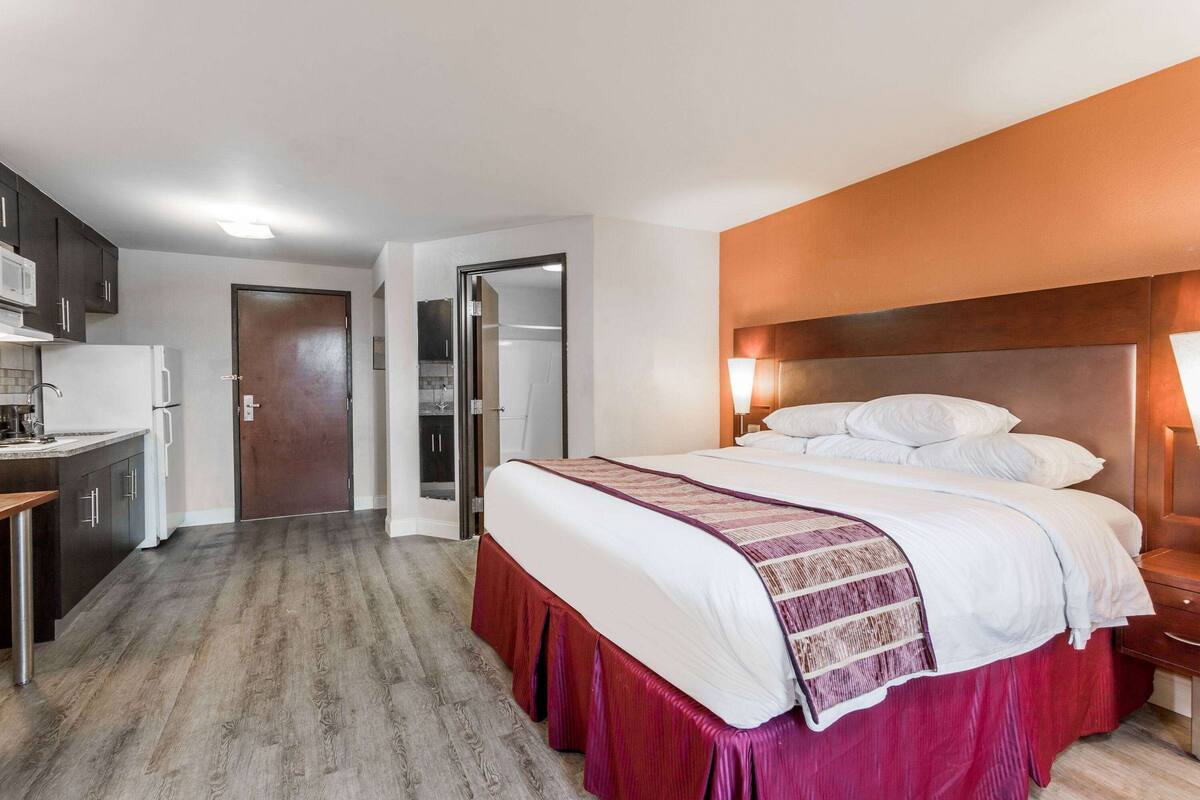 Ein Schlafzimmer mit Bett, Nachttisch und Blick auf die Küche.