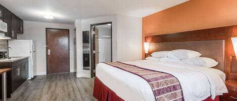 A bedroom with a bed, bedside table, and a view of the kitchen.