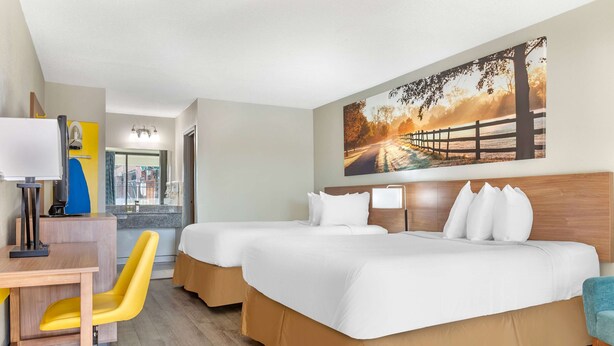 Ein Hotelzimmer mit zwei Betten, einem Schreibtisch mit Stuhl, einem großen Fenster und einem Bild an der Wand.