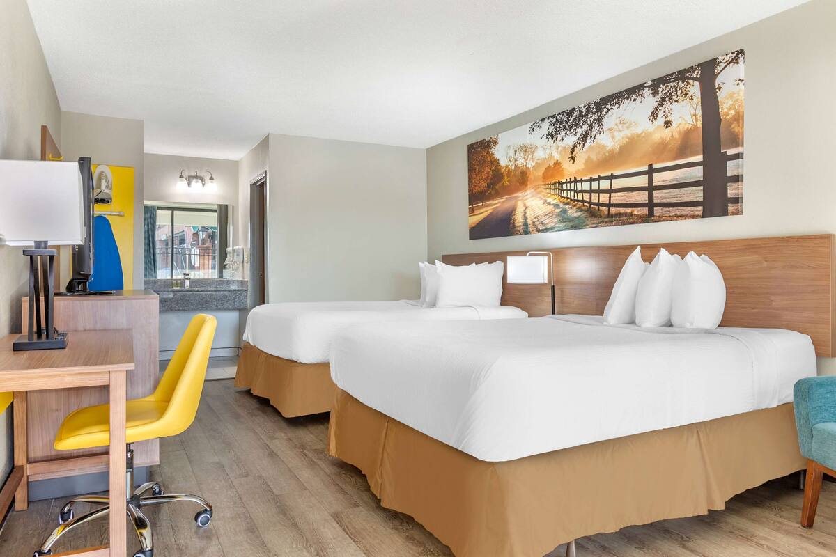 Ein Hotelzimmer mit zwei Betten, einem Schreibtisch mit Stuhl, einem großen Fenster und einem Bild an der Wand.