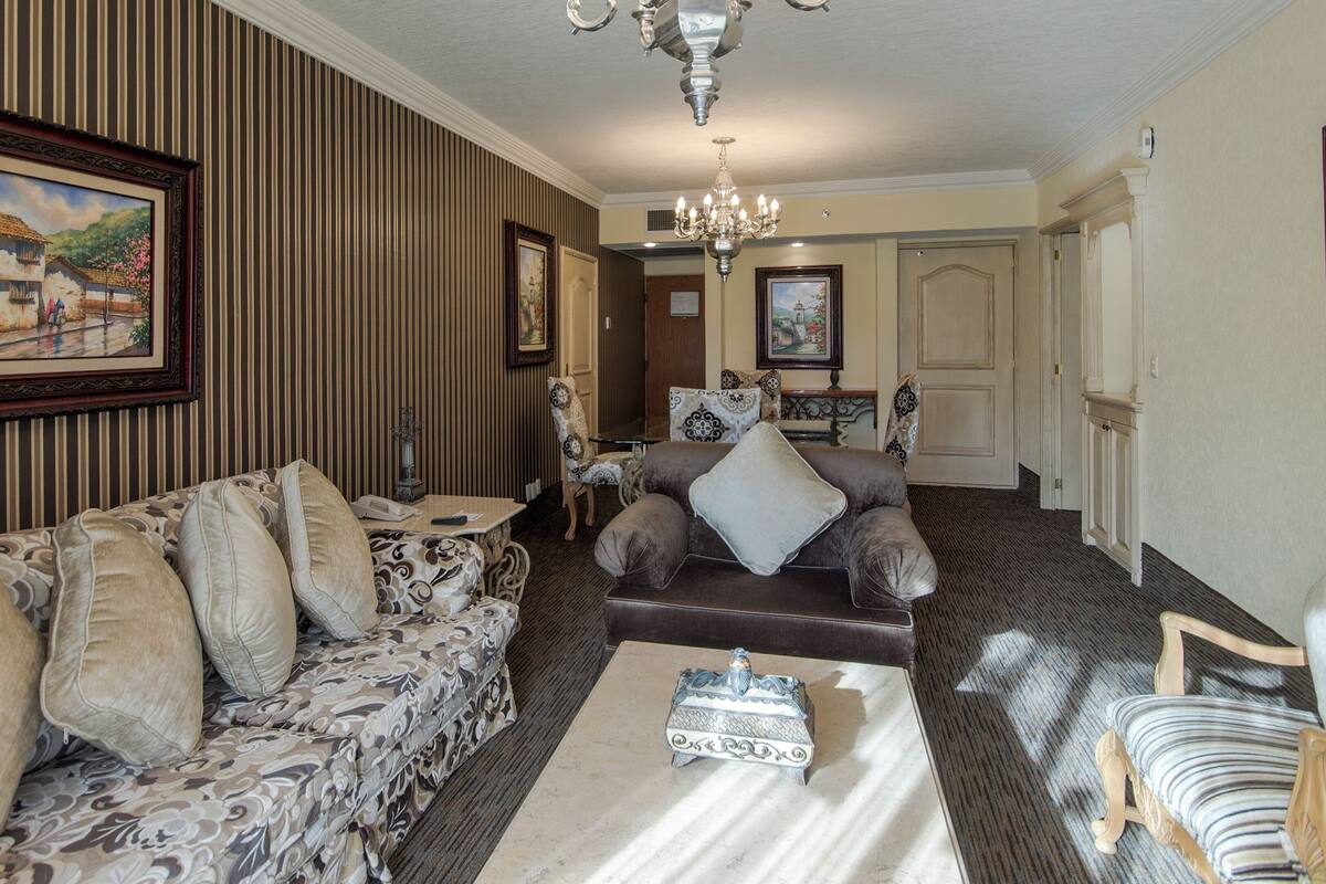 A living room with striped wallpaper, a chandelier, and a sofa with patterned cushions.