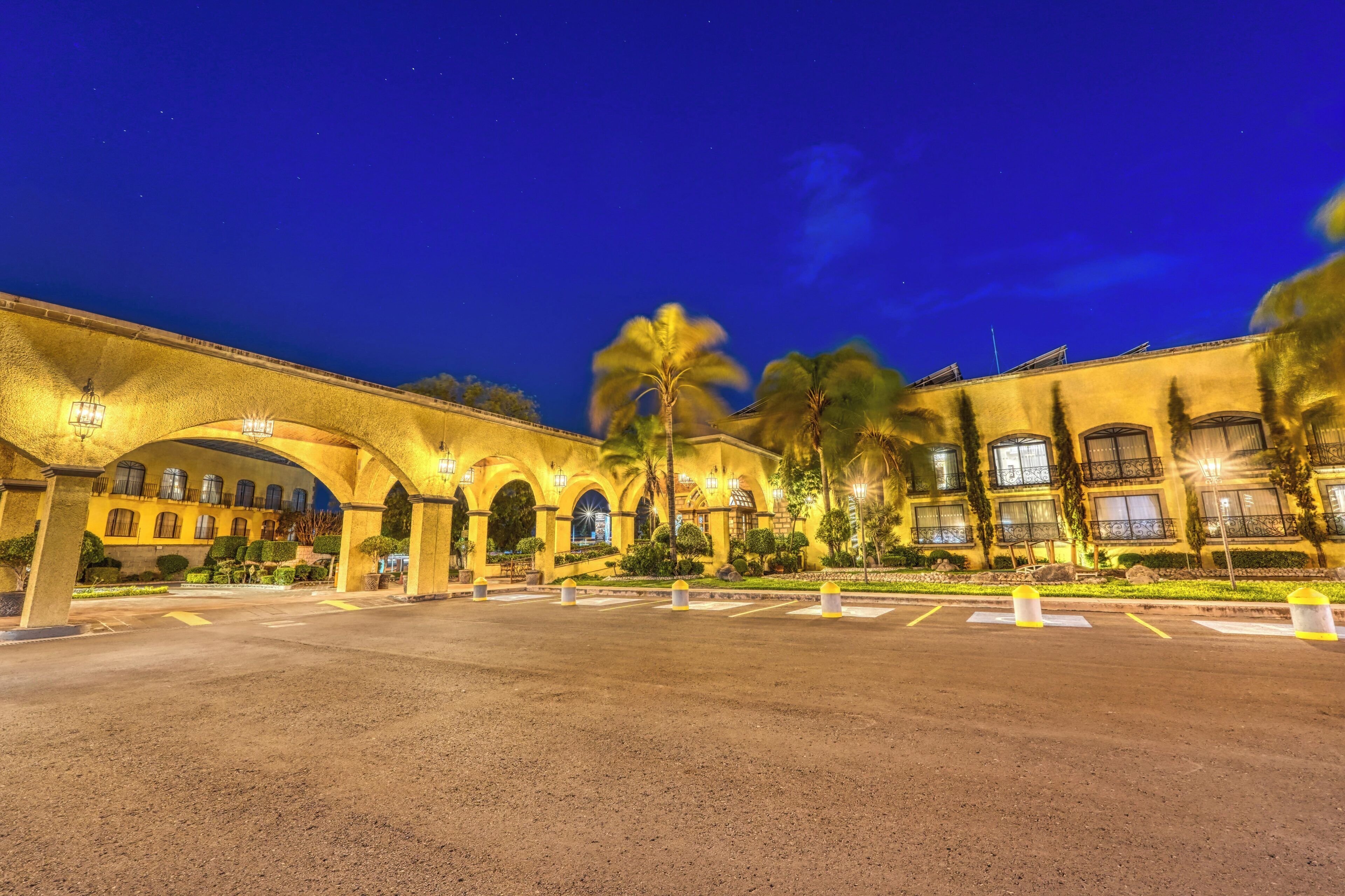 Un hotel con patio, puente de arco y palmeras.
