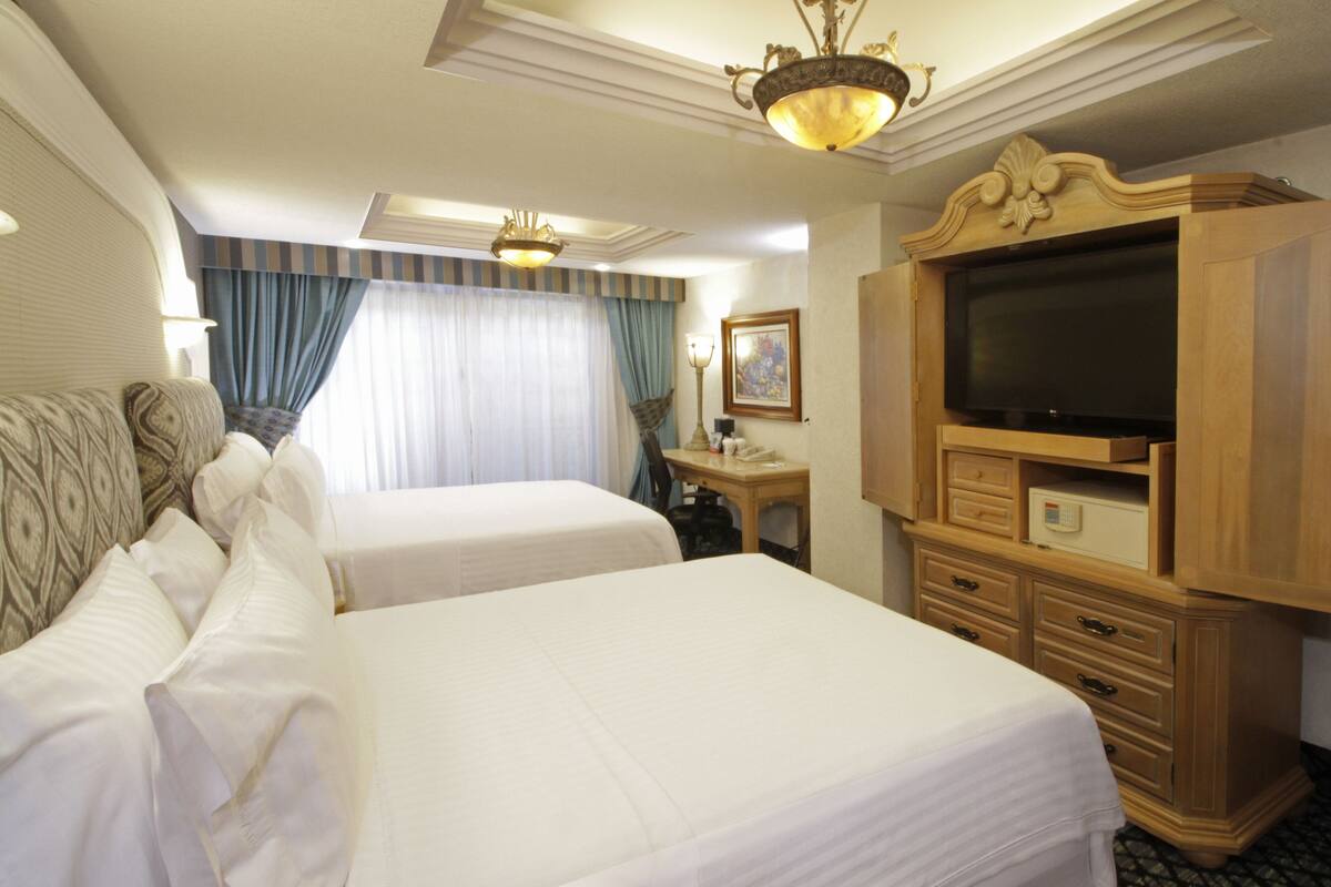 A hotel room with two beds, a television, a desk with a lamp, and a window with curtains.