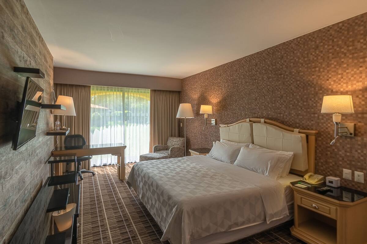 Een hotelkamer met een groot bed, een bureau met stoel, een bijzettafeltje en een lamp.