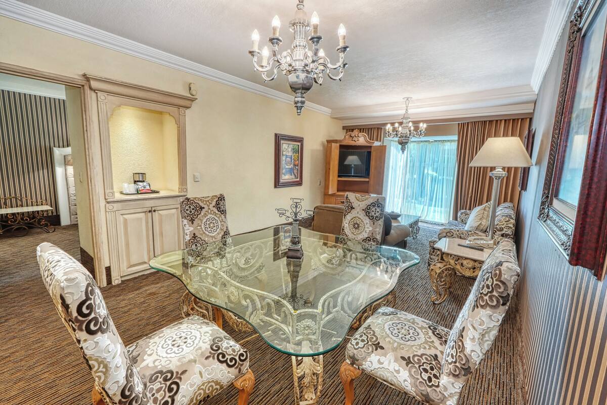 A dining area with a glass-top table, ornate chairs, a chandelier, and a sofa.