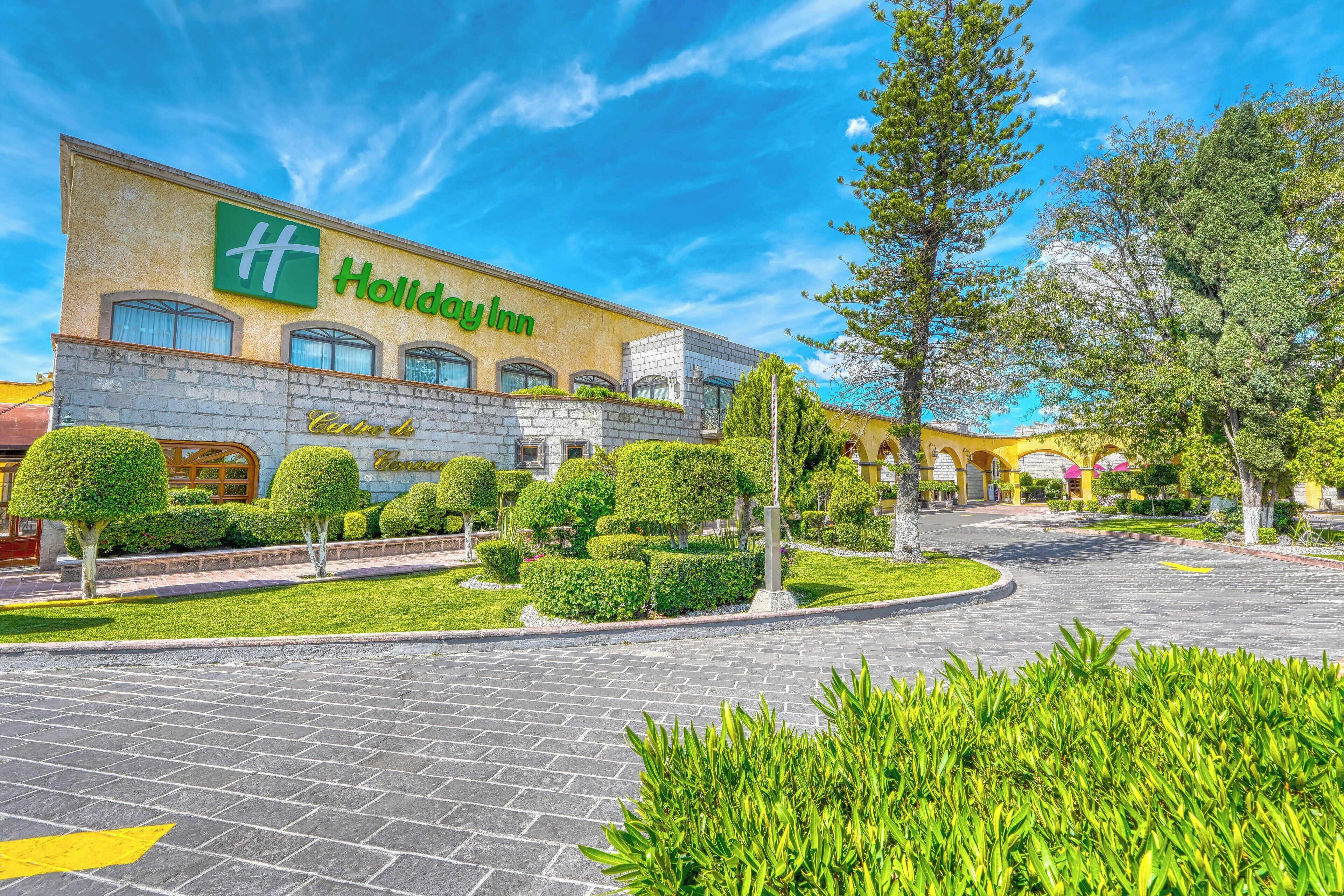 Un hotel Holiday Inn con un jardín bien cuidado y un cielo azul despejado.