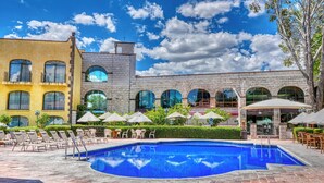 A swimming pool with lounge chairs and umbrellas, surrounded by a building with arched windows and a brick facade. - Holiday Inn Queretaro-Centro Historico by IHG (Querétaro)