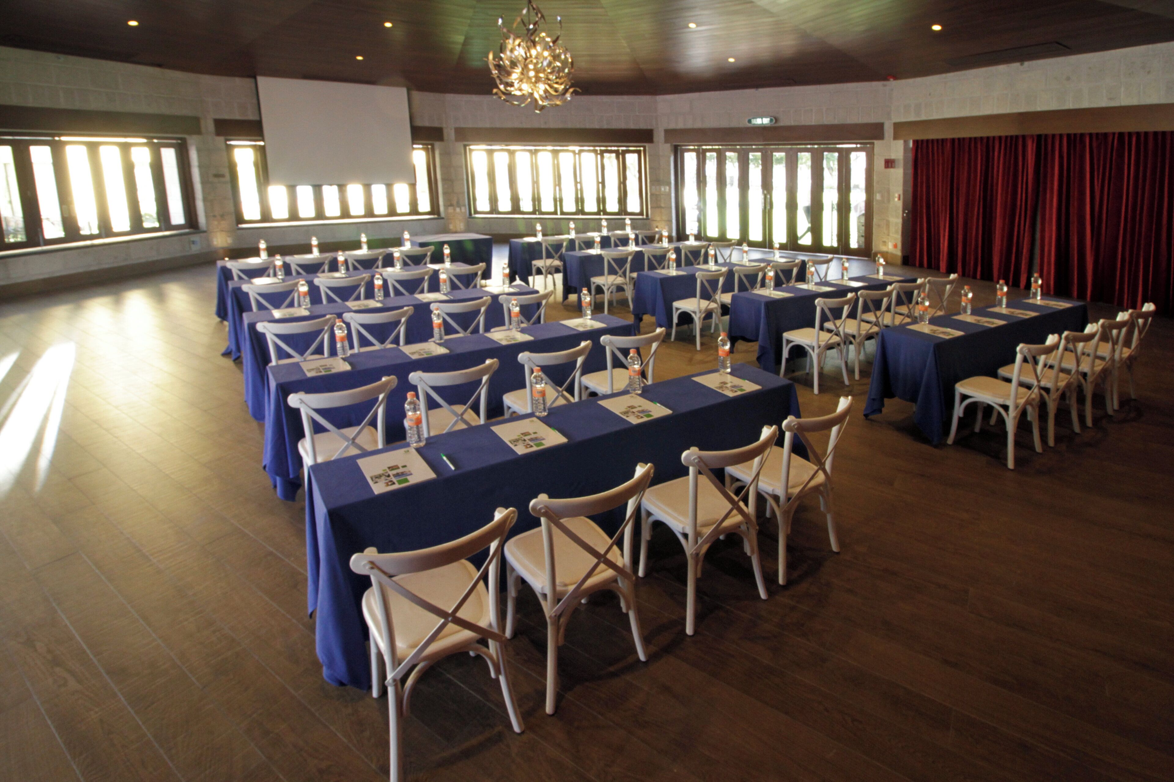 Une salle de conférence dotée de plusieurs tables et chaises, de grandes fenêtres et d’un lustre.