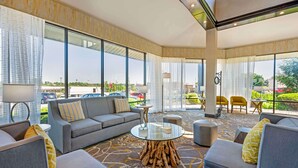 A modern hotel lobby with a grey sofa set, a glass coffee table with a wooden base, and large windows offering a view of the parking lot and greenery outside. - Best Western Ashbury Inn (La Grange)