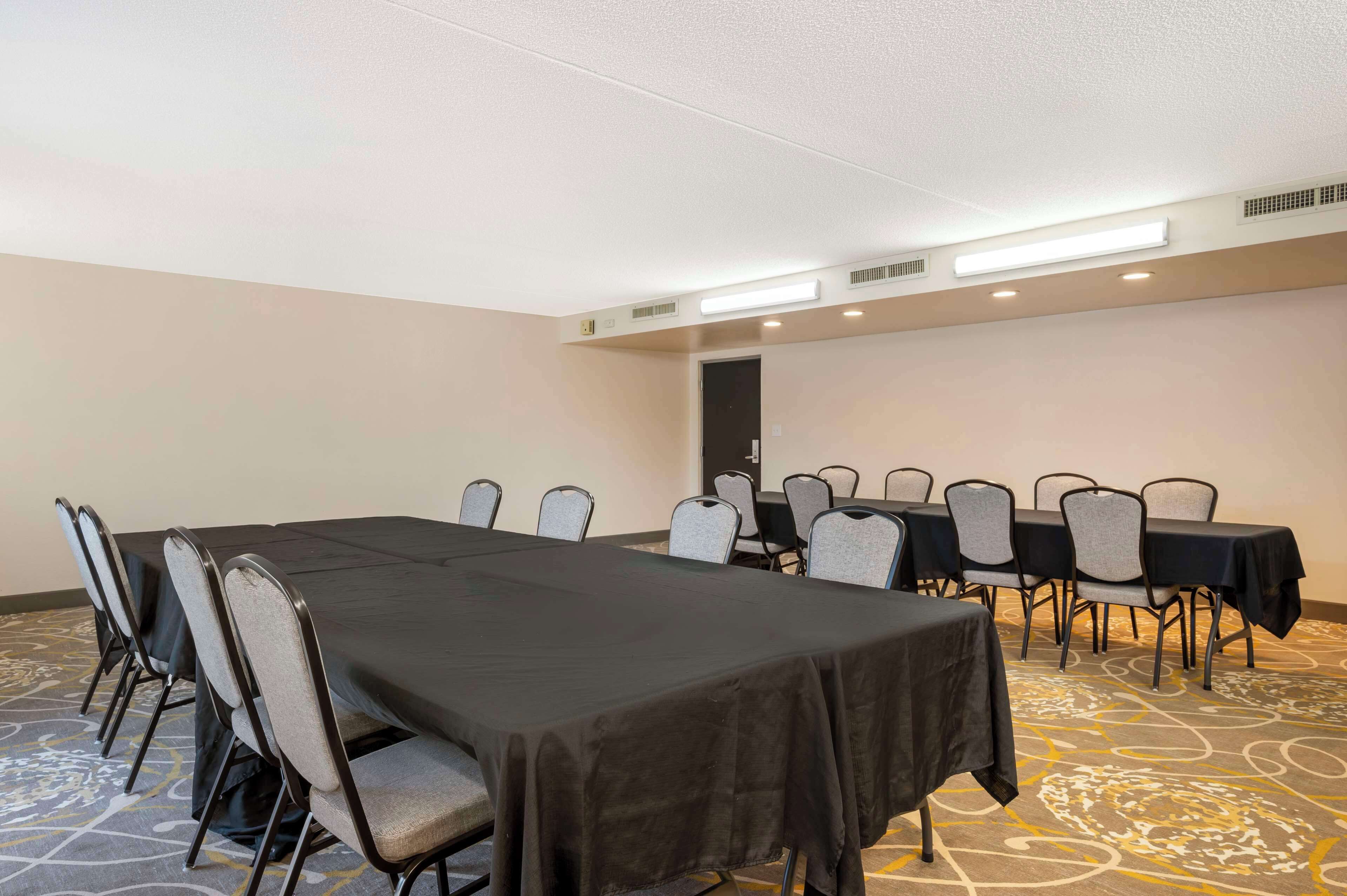 A conference room with a long table and chairs, a carpeted floor, and a door in the background.