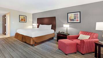 Una habitación de hotel con una cama grande, un sillón rojo, una mesita pequeña y dos lámparas de pared.