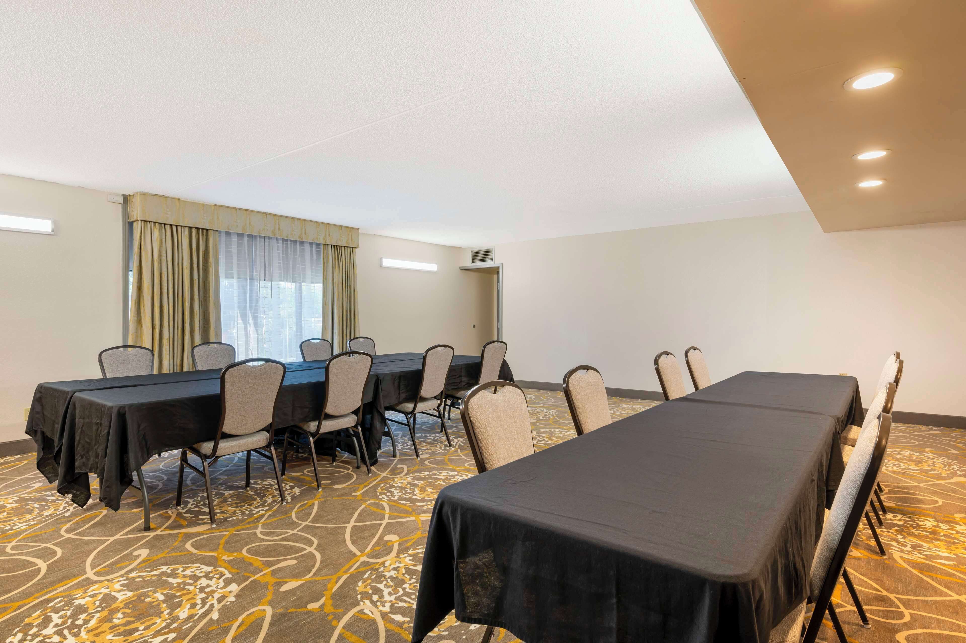 Uma sala de conferências com uma mesa comprida, cadeiras e uma janela grande com cortinas.