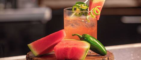 Un verre à cocktail orné d’une tranche de pastèque et d’un morceau de piment jalapeño, posé sur un sous-verre en bois.