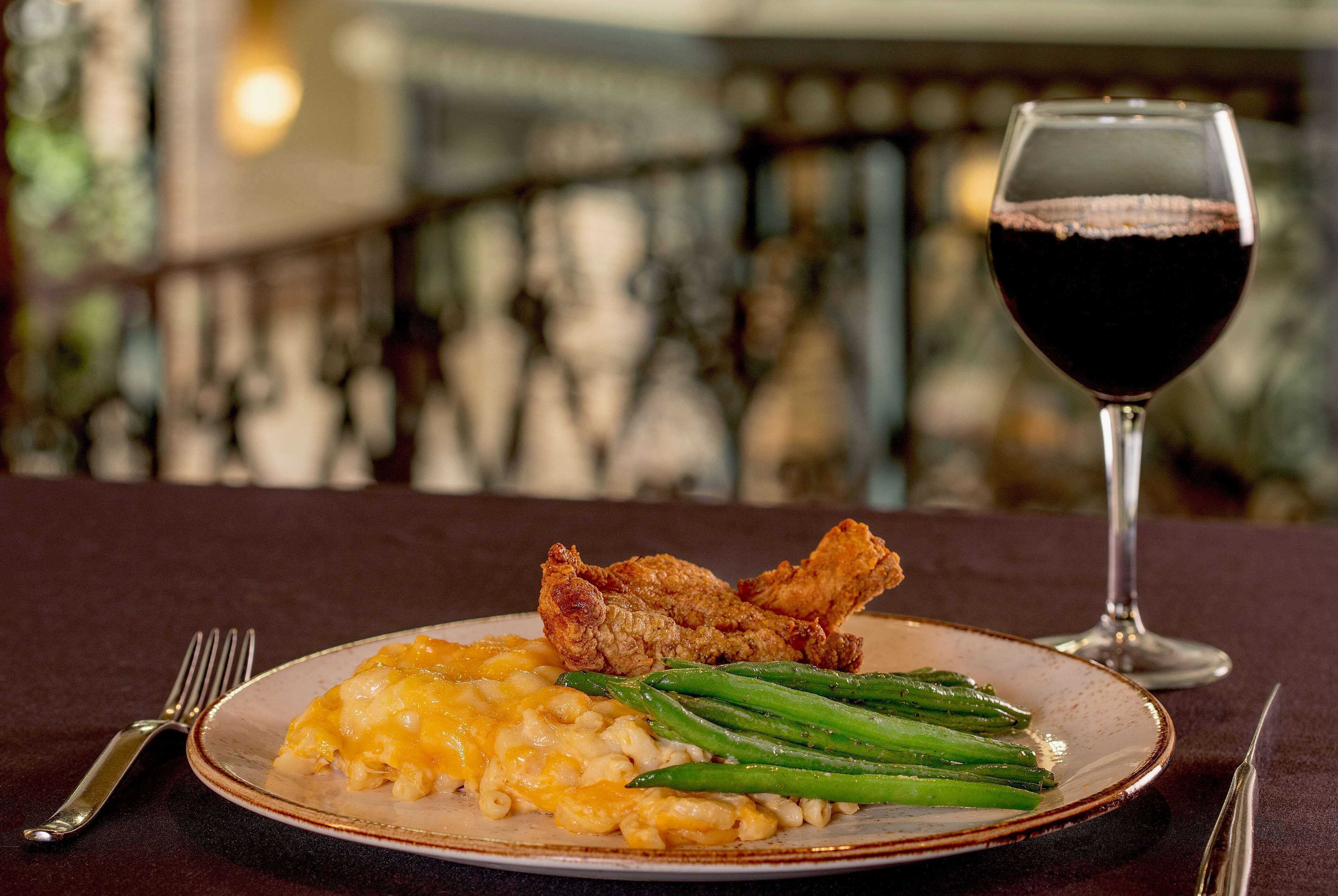 A plate of fried chicken, macaroni and cheese, and green beans with a glass of red wine on a table.